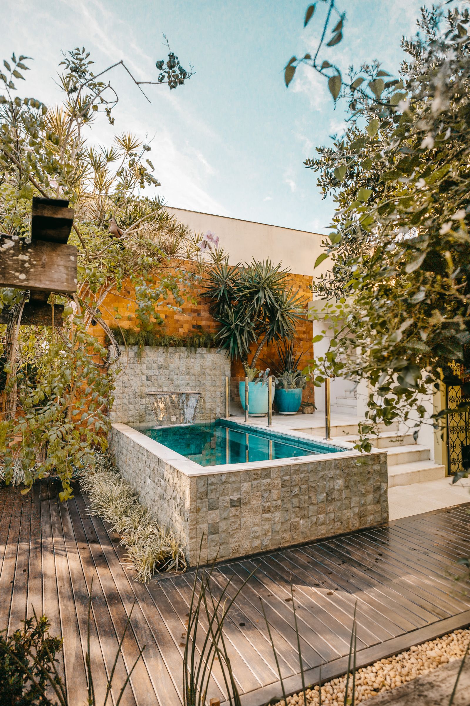 Kompaktní plunge pool s kamenným obkladem na malé zahradě s dřevěnou terasou