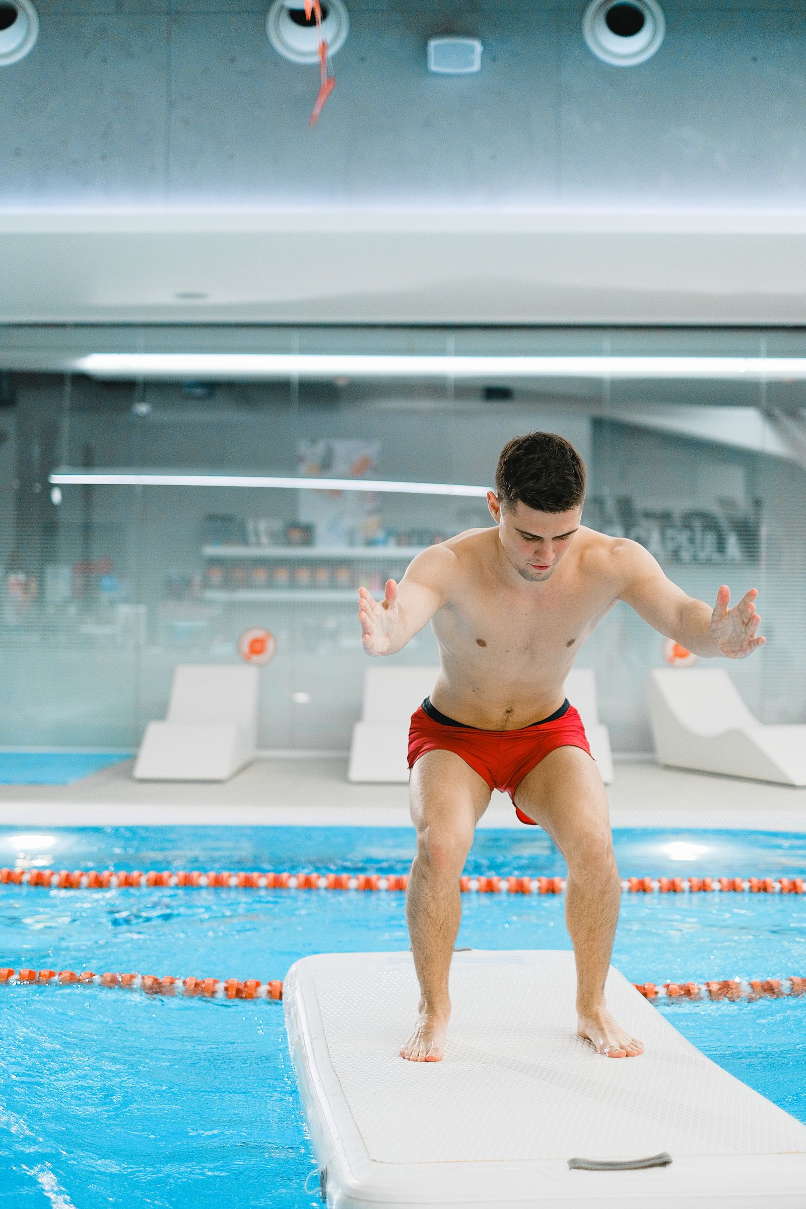 Muž cvičící ve vodě bazénu s balanční podložkou při vodním fitness tréninku