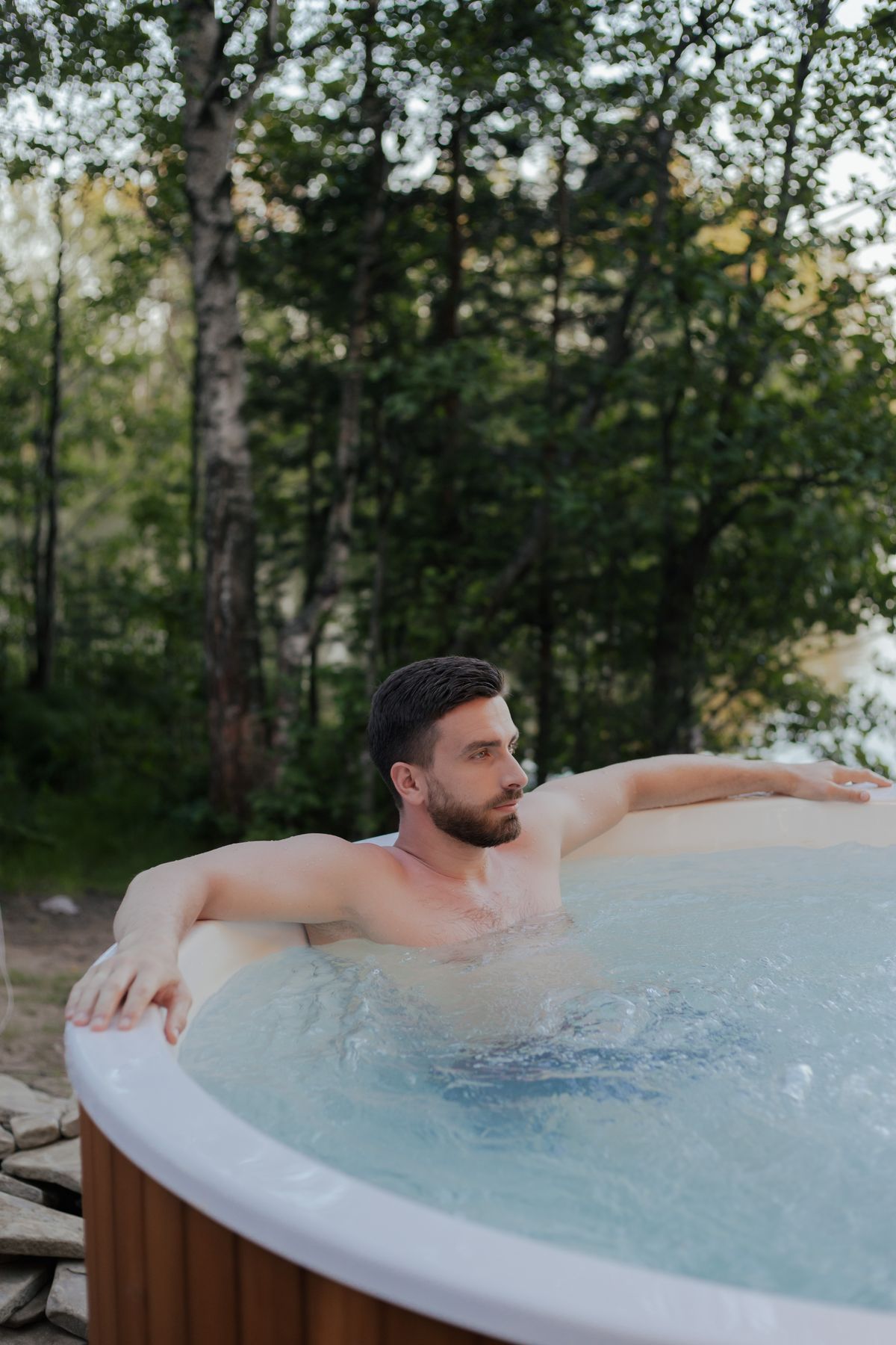 Muž relaxující ve venkovní vířivce s dřevěným opláštěním v zahradě