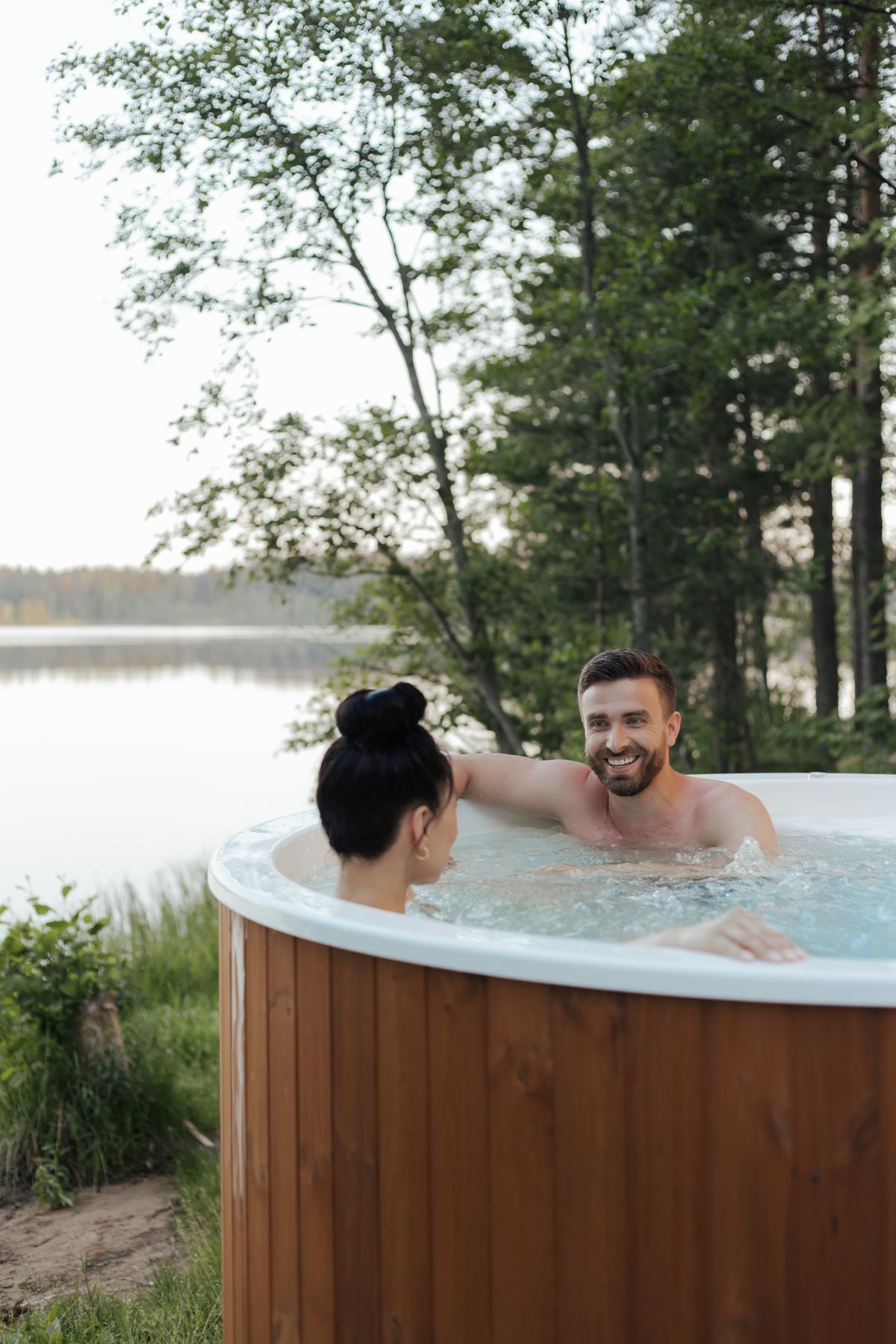 Pár relaxující ve vířivce s dřevěným kabinetem na břehu jezera