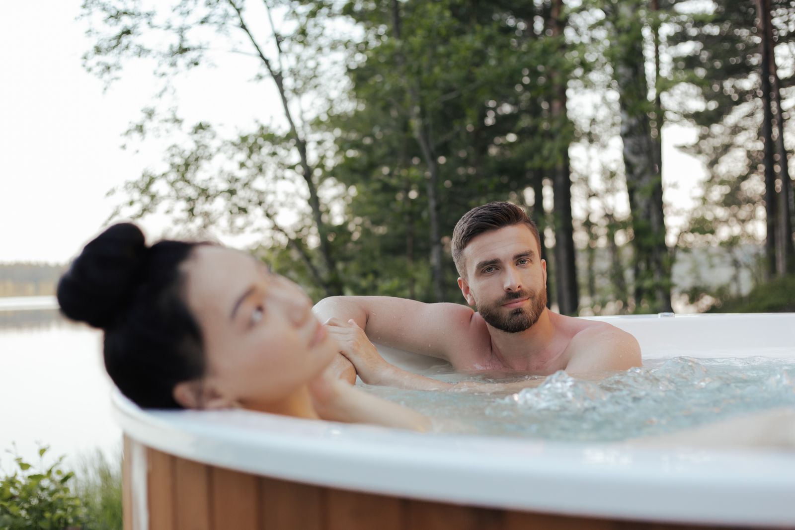 Pár hostů odpočívajících ve venkovní vířivce u lesa během wellness pobytu na chatě