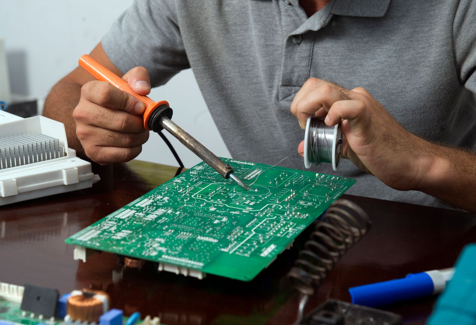Technik opravuje elektronickou desku pájecí stanicí v servisní dílně