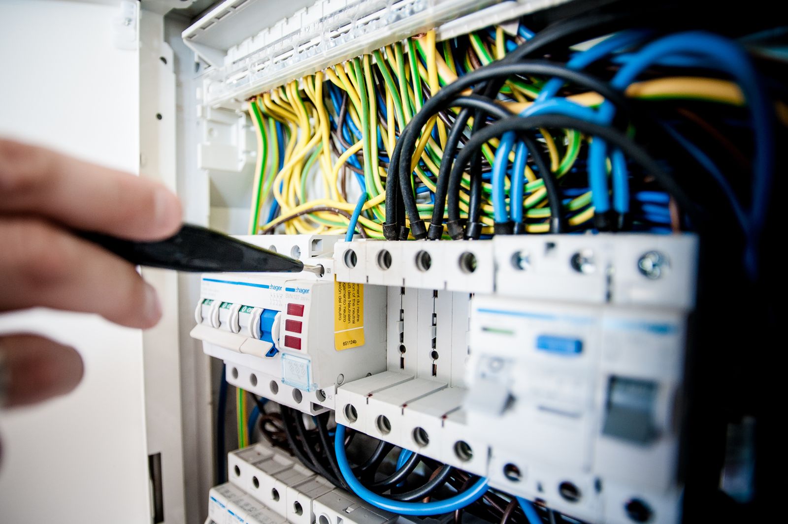 Elektrikář pracuje v otevřeném rozvaděči s jističi a vodiči