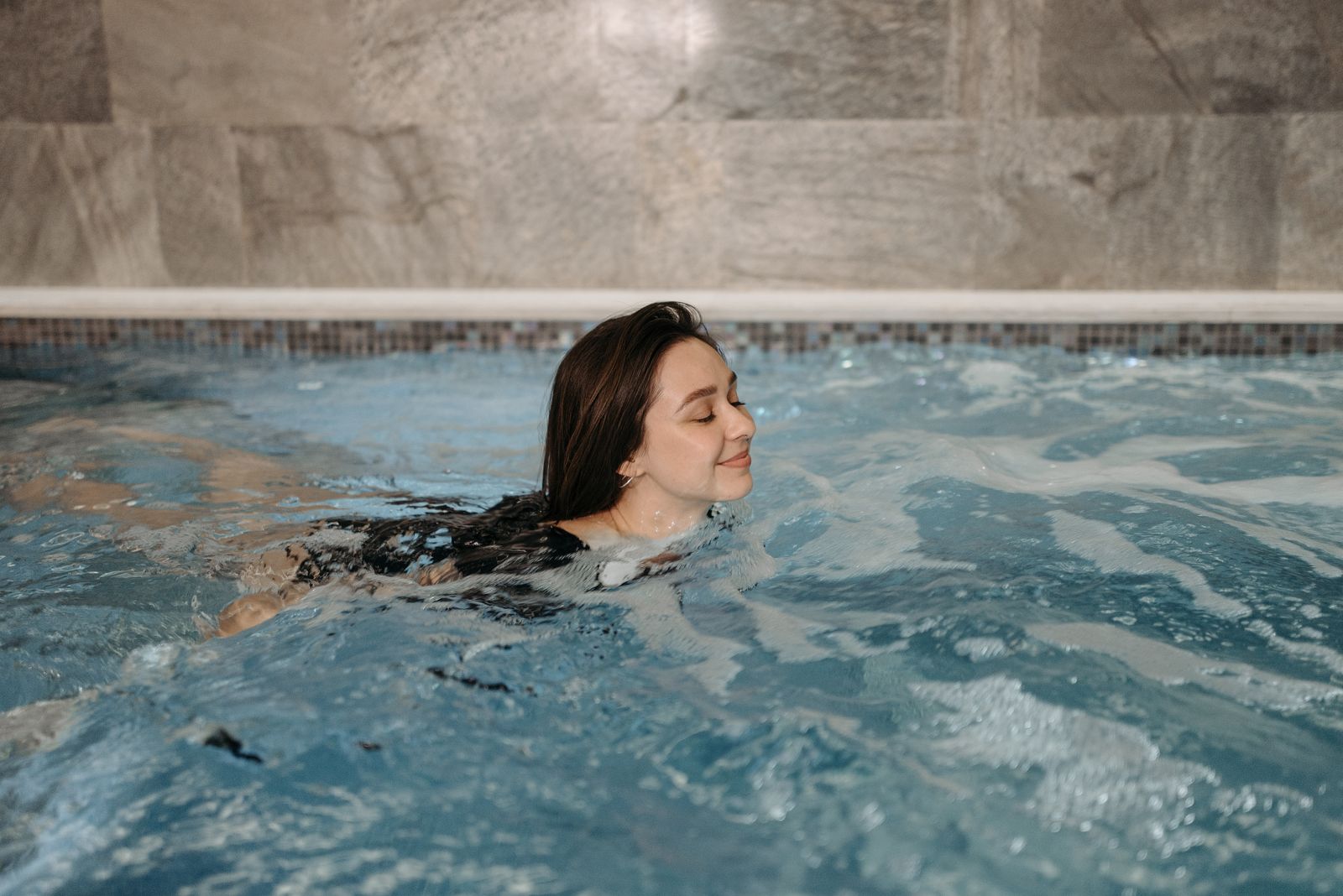 Žena plave proti proudu v kompaktním vnitřním bazénu typu swim spa