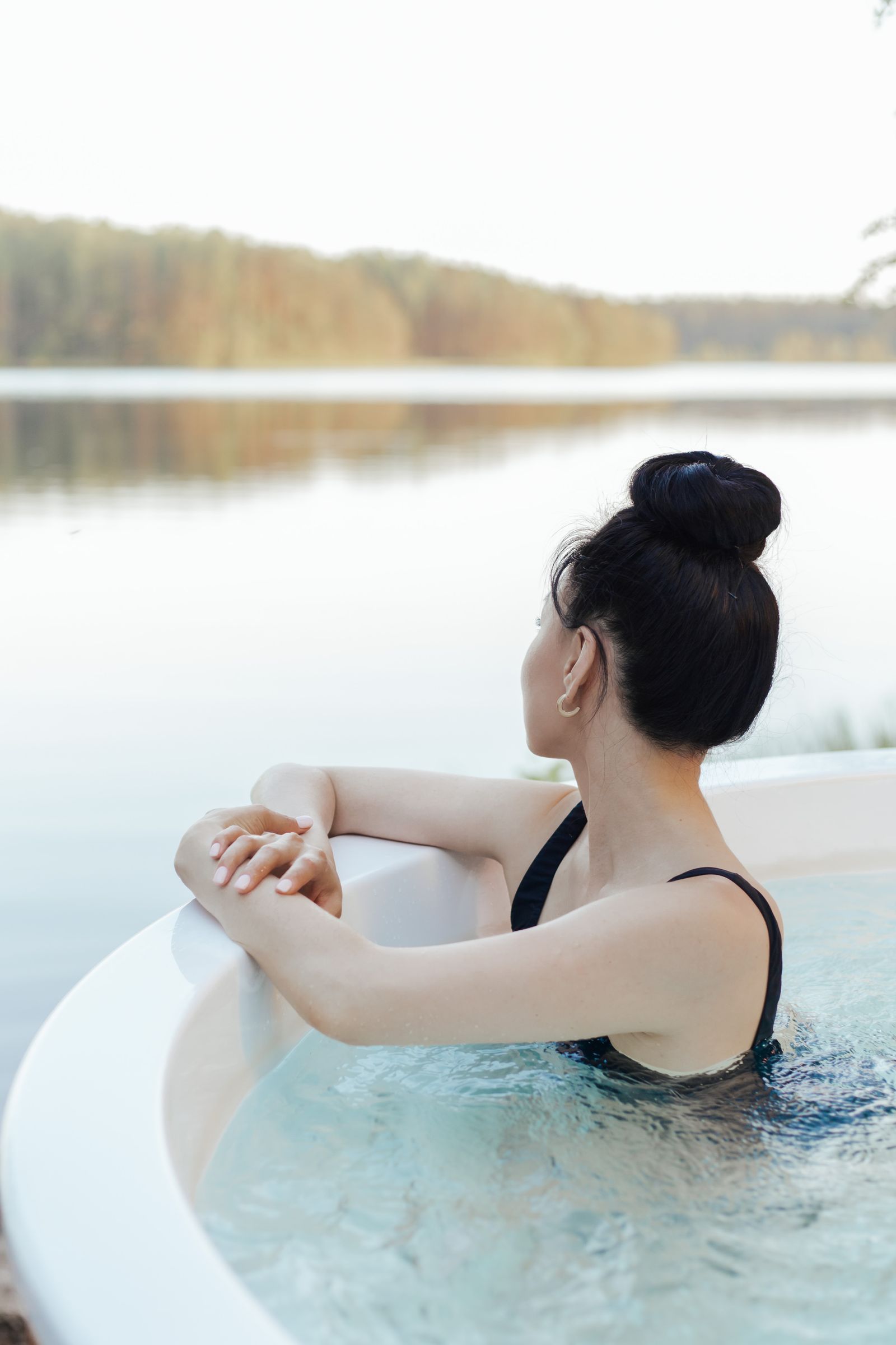 Žena odpočívá ve venkovní vířivce s výhledem na jezero a les